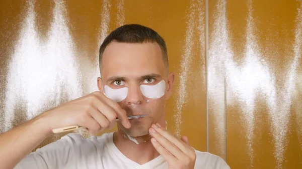 Retrato de un hombre guapo con una máscara debajo del párpado inferior, que se afeita con una navaja de afeitar en el baño. Concepto metrosexual —  Fotos de Stock