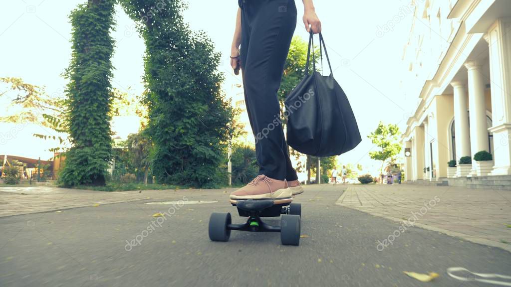 a modern business woman in a black jumpsuit in pink sneakers, sunglasses and a black bag, riding an electricboard along a city street. The concept of strange adventures of people