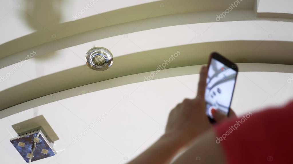 Water damage. concept of flooding the apartment and property insurance. a woman takes a photo on the phone as water drips from the ceiling of her apartment