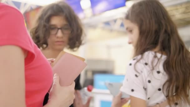 Concepto de turismo, vacaciones e intercambio de formación. Una mujer y dos adolescentes, un niño y una niña, están de pie en el aeropuerto en la taquilla para el check-in de vuelo . — Vídeo de stock