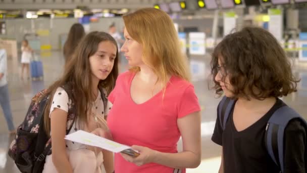 Concetto di turismo, vacanze e formazione di scambio. Una donna e due adolescenti, un ragazzo e una ragazza, sono in aeroporto alla biglietteria per il check-in . — Video Stock