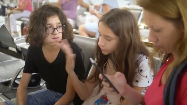 The concept of tourism, recreation and exchange learning. A woman and two teenagers, a boy and a girl, at the airport, a woman using a smartphone — Stock Video