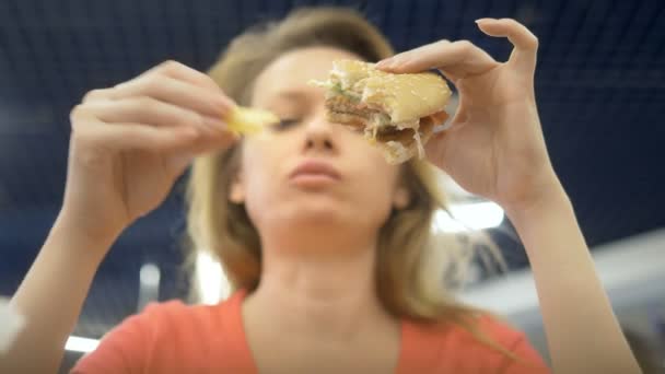 Zavřít. žena s kýchami na rtu jí hranolky a hamburger — Stock video