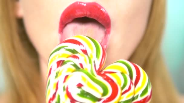 クローズアップ、赤い口紅を持つ女性の唇は、食べて、心臓の形で大きなロリポップを舐める. — ストック動画