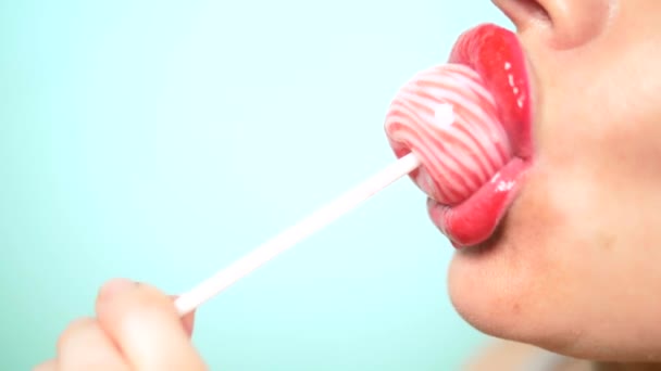 Close-up, female sexy lips with red lipstick suck big pink round lollipop. copy space. blue background — Stock Video