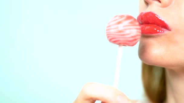 Zbliżenie, kobiece seksowne usta z czerwoną szminką ssać duży różowy okrągły lizak. przestrzeni kopiowania. niebieskie tło — Wideo stockowe