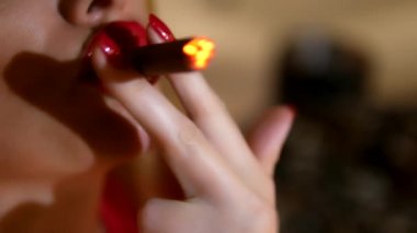 karanlık bir arka planda bir puro ile dudakları ve koyu gözlük kırmızı ruj ile kırmızı elbise güzel kadın. Ağzından kalın duman üretir