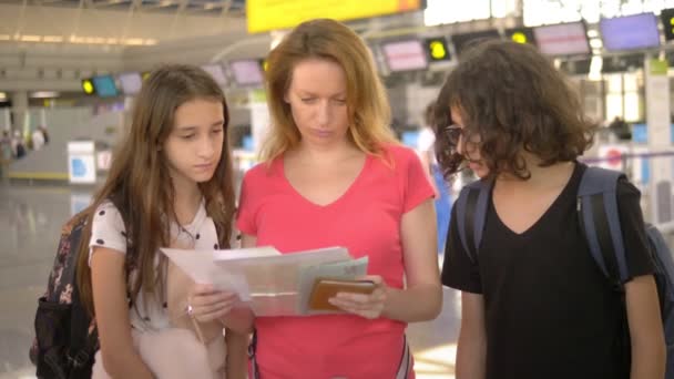 Concepto de turismo, vacaciones e intercambio de formación. Una mujer y dos adolescentes, un niño y una niña, están de pie en el aeropuerto en la taquilla para el check-in de vuelo . — Vídeos de Stock