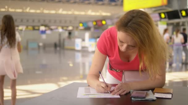 Konzept der Beförderung eines unbegleiteten Kindes. Eine Frau mit zwei halbwüchsigen Kindern füllt am Flughafen Dokumente aus — Stockvideo