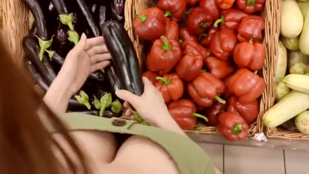 Woman chooses eggplants at the counter with vegetables in the store. view from above — Stock Video