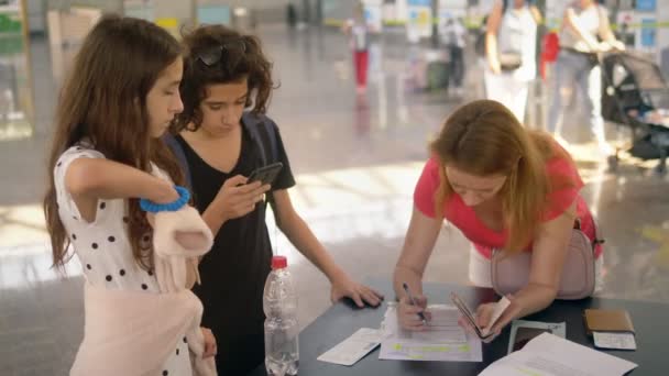 Conceito de transporte de uma criança não acompanhada. Uma mulher com dois filhos adolescentes preenche documentos no aeroporto — Vídeo de Stock
