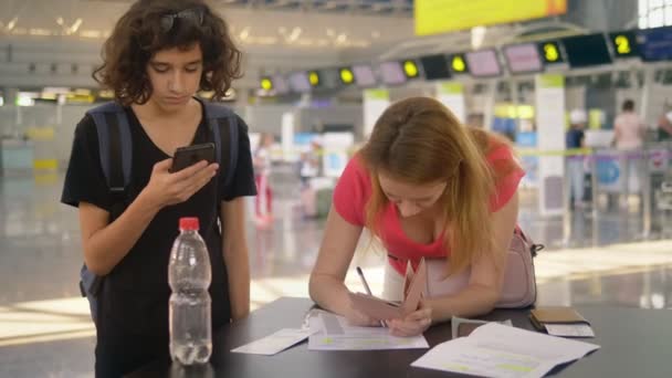 同伴者のいない子供の輸送の概念。2人の十代の子供を持つ女性が空港で書類に記入する — ストック動画