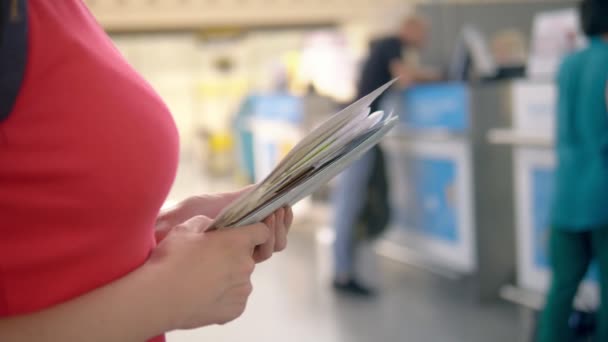 El concepto de turismo, recreación. Una mujer está de pie en el aeropuerto en la taquilla para el check-in, sosteniendo documentos en sus manos — Vídeos de Stock