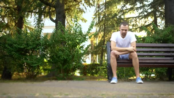 Depressiver, trauriger junger Mann, der allein auf einer Bank in einem Sommerpark sitzt. Kopierraum — Stockvideo