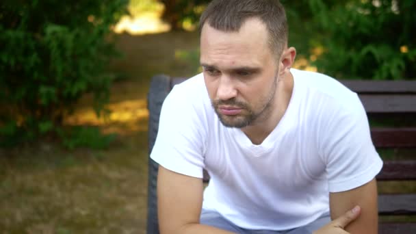 Przygnębiony Sad młody człowiek siedzi samotnie na ławce w letnim parku. miejsce kopiowania — Wideo stockowe
