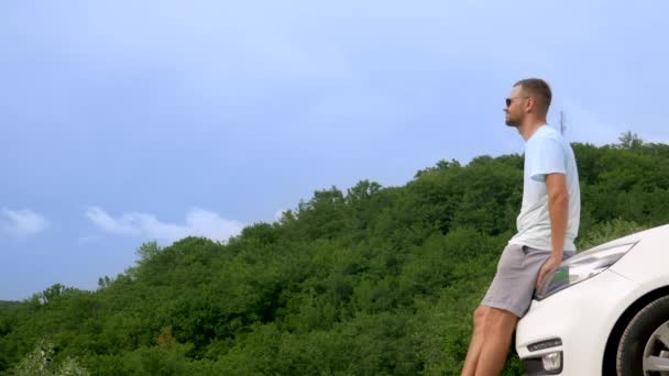 Summer car travel to freedom. handsome man in with hands up, cheerful and happy against the blue sky and mountains. Summer trip traveler concept — Stock Video