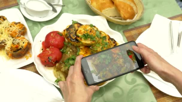 Las manos femeninas hacen fotos en un smartphone en un restaurante con platos de cocina caucásica. verduras a la parrilla, shashlik, salsa — Vídeos de Stock
