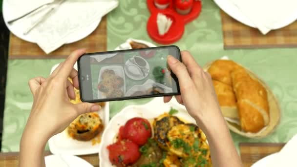 Las manos femeninas hacen fotos en un smartphone en un restaurante con platos de cocina caucásica. verduras a la parrilla, shashlik, salsa — Vídeos de Stock