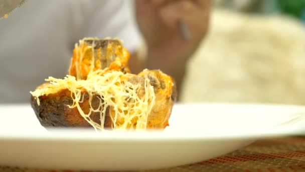 Alguém corta um cogumelo cozido a segurar um garfo. close-up. Cogumelos recheados com queijo e verduras . — Vídeo de Stock
