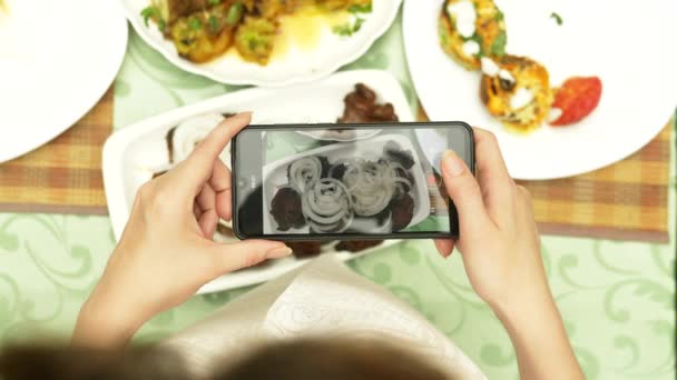 Las manos femeninas hacen fotos en un smartphone en un restaurante con platos de cocina caucásica. verduras a la parrilla, shashlik, salsa — Vídeos de Stock