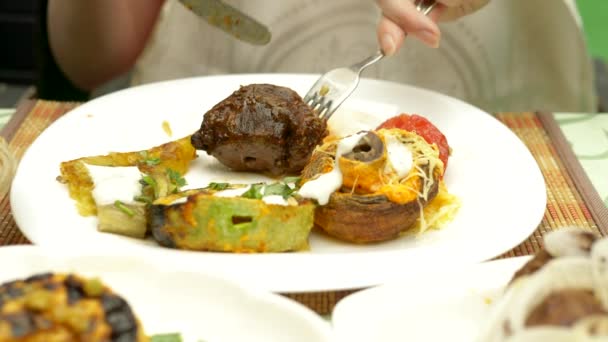 Legumes grelhados fechar em um restaurante. Mulher come com uma faca e garfo legumes grelhados e shish kebab — Vídeo de Stock