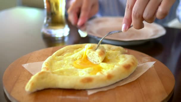 Κοντά γυναικεία χέρια με ένα μαχαίρι και ένα πιρούνι κόβουν ένα κομμάτι από την Αζαρά κατσούρι με ένα αυγό σε ένα πιάτο σε ένα εστιατόριο. Γεωργιανό εθνικό φαγητό — Αρχείο Βίντεο