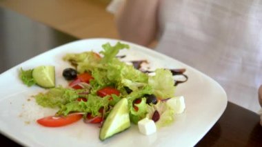 Çatalla kadın ellerinin yakın çekim. Bir kafede lezzetli Yunan salatası yiyen kadın