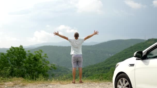 Το καλοκαιρινό αυτοκίνητο ταξιδεύει στην ελευθερία. όμορφος άντρας με τα χέρια ψηλά, χαρούμενο και χαρούμενο εναντίον του γαλάζιου ουρανού και των βουνών. Καλοκαιρινή εκδρομή — Αρχείο Βίντεο