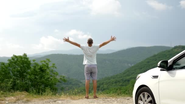 Verano viaje en coche a la libertad. hombre guapo en con las manos en alto, alegre y feliz contra el cielo azul y las montañas. Viaje de verano viajero concepto — Vídeos de Stock