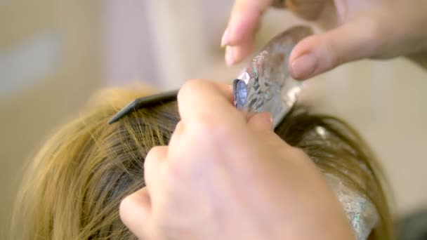 Primer plano. Teñido de pelo en la peluquería. manos de un peluquero teñir hebras de cabello y envolver en papel de aluminio, peluquero profesional que trabaja con el cliente en el salón . — Vídeos de Stock