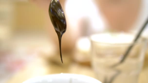 特写。液体将巧克力从勺子滴入杯子中。咖啡馆里的热巧克力 — 图库视频影像
