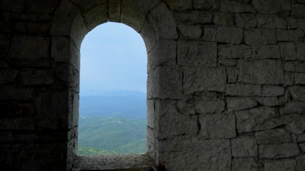 Parede de pedra e aberturas de janelas arqueadas com vista para uma cordilheira com floresta e neblina sobre as montanhas — Vídeo de Stock