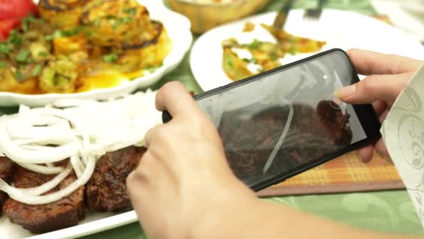 Kvinnliga händer gör foto på en smartphone i en restaurang med rätter av kaukasiska köket. grillade grönsaker, Shashlik, sås — Stockvideo