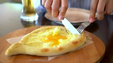 Bir bıçak ve çatal ile yakın kadın elleri bir restoranda bir tabak üzerinde bir yumurta ile Acara khachapuri bir dilim kesti. Gürcü ulusal gıda