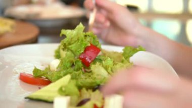 Çatalla kadın ellerinin yakın çekim. Bir kafede lezzetli Yunan salatası yiyen kadın