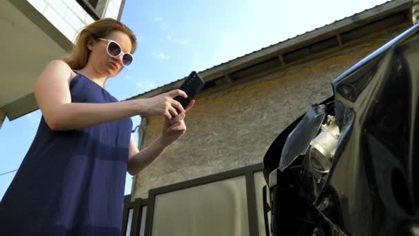 A woman takes a photo on her smartphone after the crash of a broken car bumper — Stock Video