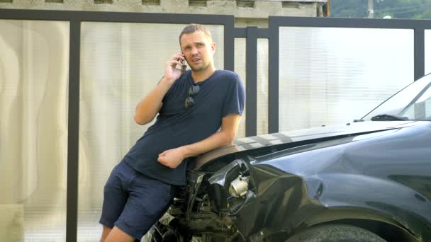 Conceito de acidente de carro. homem em estado de choque falando ao telefone após um acidente de carro, em pé junto a um carro com um pára-choques quebrado — Vídeo de Stock