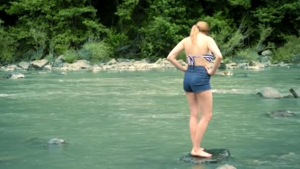 Концепція літніх канікул. жінка в купальнику і шорти переходить через гірську річку до броду — стокове відео
