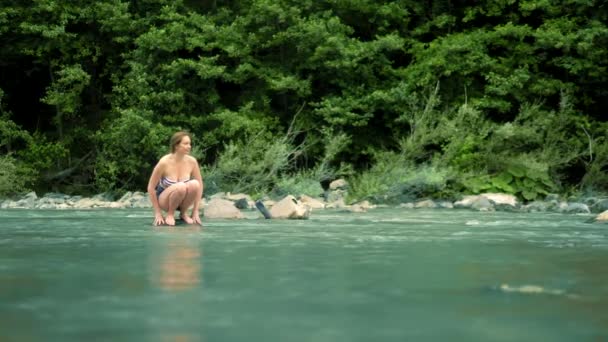 Летние каникулы. женщина в купальнике и шортах идет по горной реке к броду — стоковое видео