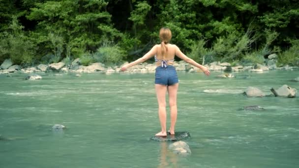 Zomer vakantie concept. een vrouw in een badpak en shorts gaat over een berg rivier naar een Ford — Stockvideo