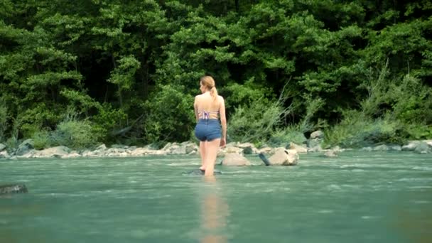 Sommarsemester koncept. en kvinna i baddräkt och shorts går över en fjäll flod till en Ford — Stockvideo