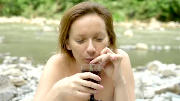 Una donna a un picnic vicino al fiume beve un drink attraverso una piuma di cipolla verde e lo mangia dopo — Video Stock