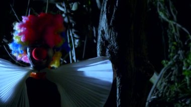 Cadılar Bayramı, geceleri korkunç bir karanlık ormanda boynunda bir yay ile kötü palyaço. yıldırım yanıp söner