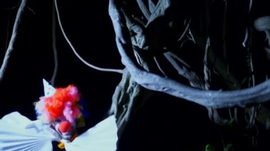 Cadılar Bayramı, geceleri korkunç bir karanlık ormanda boynunda bir yay ile kötü palyaço. yıldırım yanıp söner