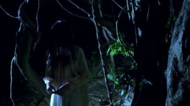 Halloween. uzun siyah yüz saçlı hayalet kız yıldırım flaş kalın bir korkunç ormanda duruyor.