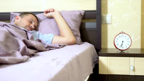 Хлопець у блакитній піжамі прокидається вранці і радіє пробудженню, вимикає тривогу — стокове відео
