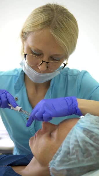 수직 비디오. 화장품 개념. 코 윤곽 보정. 의사 미용사가 환자 여성의 코에 필러를 주입합니다. 클로즈업 — 비디오