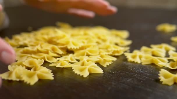 Rå pasta. Farfalle närbild. Kvinnliga händer samla pasta från ett träbord. — Stockvideo