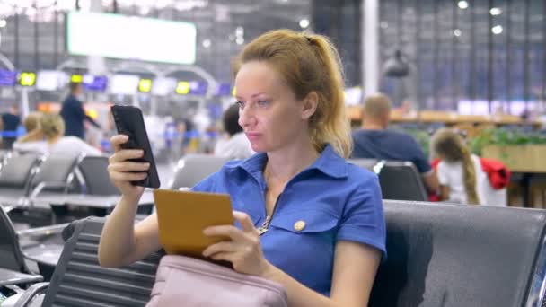 Frau am Flughafen im Wartezimmer. Mädchen sitzt mit Smartphone und hält Reisepass mit Gepäck. — Stockvideo