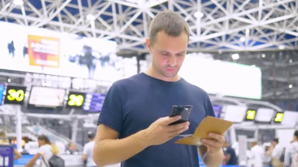 Stilig man på flygplatsen i väntrummet. man sitter använder en smartphone och innehar ett pass — Stockvideo